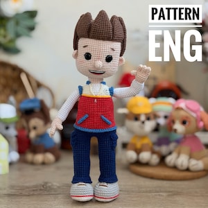 May include: A handmade crochet doll of a cartoon character, dressed in a red vest, blue trousers, and white shoes. The doll has brown hair and is waving. The text "PATTERN ENG" is visible. Other similar dolls are in the background.