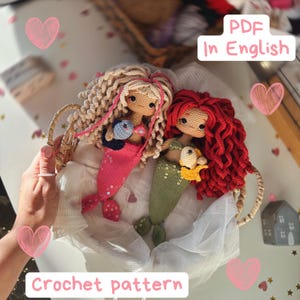 Puede incluir: Dos muñecas sirena de ganchillo hechas a mano con pelo de lana, una con pelo rubio y cola rosa, la otra con pelo rojo y cola verde, cada una sosteniendo un pequeño pez. La imagen incluye el texto PDF In English y Crochet pattern.