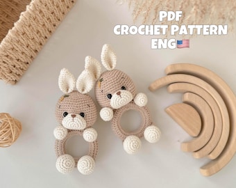 May include: Two crocheted bunny rattle toys with beige fur and white ears. The toys have a ring in the middle and are perfect for babies to play with.