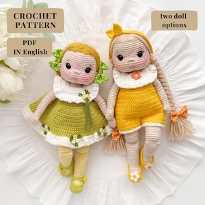 Puede incluir: Dos muñecas de ganchillo hechas a mano. Una muñeca viste un vestido verde con cuello blanco, la otra viste un pelele amarillo. Ambas muñecas tienen pelo de hilo, lazos y están sobre una superficie blanca. El texto de la imagen dice "CROCHET PATTERN PDF IN English" y "two doll options."