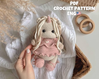 May include: Crochet pattern PDF for a unicorn amigurumi doll wearing a pink dress. The doll is made with white yarn and has a pink heart on its chest. The pattern is in English.