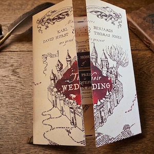 May include: A gatefold wedding invitation featuring a cream-colored parchment design with dark brown ink illustrations of a castle, winding paths, and the text Karl David Hurst and Benjamin Thomas Jones are proud to present their wedding.