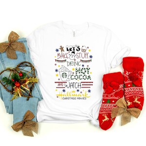 Könnte beinhalten: Ein weißes T-Shirt mit dem Text "Let's Bake & Stuff, Drink Hot Cocoa, and Watch Hallmark Christmas Movies" wird mit blauen Jeans, roten Weihnachtssocken und dekorativen Schleifen kombiniert, was ein festliches Urlaubsthema ergibt.