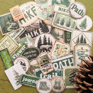 May include: A collection of vintage-style outdoor-themed stickers and labels. The designs feature images of trees, mountains, bears, deer, and hiking boots, with phrases like "Hike," "Path," and "Wander. Hike. Repeat." The color palette includes green, brown, and white.