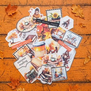May include: A collection of autumn-themed stickers featuring illustrations of books, pumpkins, coffee cups, candles, and people reading. The stickers include text such as Just another chapter, books and pumpkins, autumn reading, and autumn leaves.