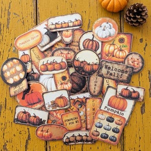 May include: A collection of fall-themed decorative stickers featuring pumpkins, sunflowers, and the text "Pumpkin Spice" and "Welcome Fall!". The stickers are in various shapes and sizes, with a rustic, vintage aesthetic.