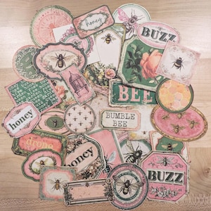 May include: A collection of vintage-style paper ephemera with bee and honey-themed designs. The pieces feature pink, green, and cream colors, with illustrations of bees, flowers, and text like "honey" and "buzz".