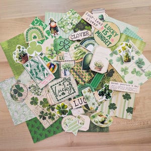 May include: A collection of St. Patrick's Day themed paper ephemera, including stickers, tags, and patterned papers. The designs feature shamrocks, leprechauns, and phrases like "Lucky is a Mindset" and "Clover". The color palette is primarily green and white.