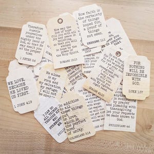 May include: A collection of vintage-style paper tags with rounded corners. Each tag features printed inspirational quotes and Bible verses in black ink. The tags are beige and have a hole at the top for hanging.