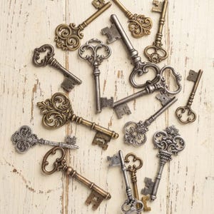 May include: An assortment of antique keys in various sizes and designs, including ornate scrollwork and simple shapes. The keys are in shades of gold, silver, and bronze, scattered on a distressed, light-colored wooden surface.