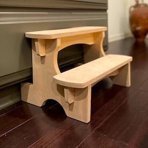 May include: A light wood step stool with two steps. The stool is made of natural wood and has a simple design.
