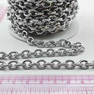 Peut inclure: Une chaîne argentée brillante avec des maillons ronds. Une section de la chaîne est posée à plat à côté d'une règle rose. La chaîne est en métal et convient à la fabrication de bijoux ou à l'artisanat.