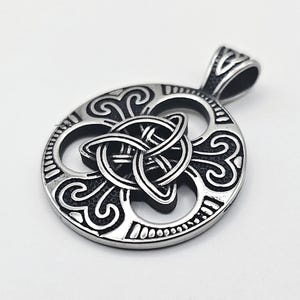 Può includere: Ciondolo color argento con un design a nodo celtico. Il ciondolo presenta una cornice circolare con motivi intricati e un nodo centrale. L'anello è integrato nel design. Il ciondolo è mostrato su sfondo bianco.