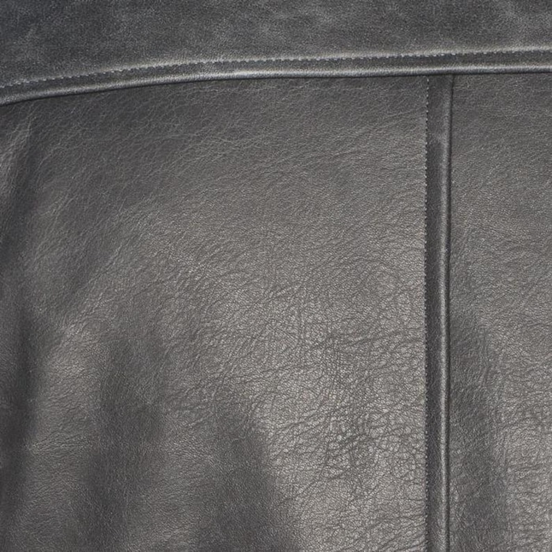 Peut inclure: Gros plan sur une section de cuir gris fonc&eacute;. Le cuir pr&eacute;sente une surface textur&eacute;e avec un grain visible et de subtiles variations de couleur. Une couture horizontale et une couture verticale sont visibles.