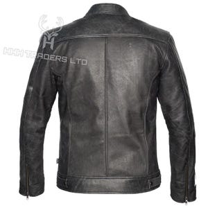 Peut inclure: Veste en cuir noir vieilli, de conception classique. Elle pr&eacute;sente un col montant, des manches zipp&eacute;es et un aspect us&eacute;. La vue arri&egrave;re montre la coupe ajust&eacute;e de la veste et le logo "HHH TRADERS LTD".