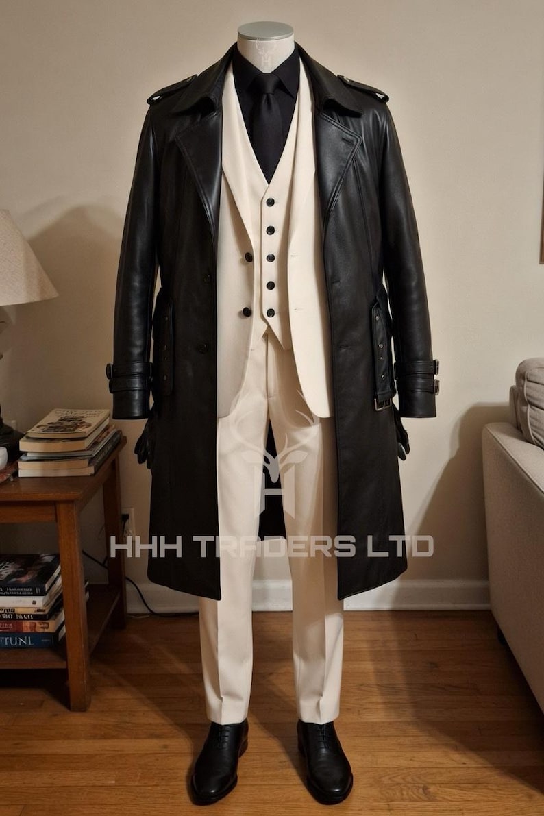 Puede incluir: Un abrigo largo de cuero negro, un traje color crema y una corbata negra se exhiben en un maniqu&iacute;. El traje incluye un chaleco y pantalones. El texto "HHH TRADERS LTD" es visible. Zapatos negros completan el conjunto.