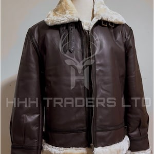Pode incluir: Casaco de couro castanho com gola e forro de pele de carneiro creme. O casaco tem fecho de correr e um log&oacute;tipo no peito. O texto "HHH TRADERS LTD" &eacute; exibido na parte superior e inferior do casaco.