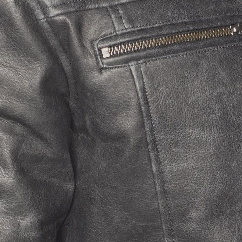 Peut inclure: Gros plan sur une veste en cuir noire. La veste a une surface textur&eacute;e avec des coutures visibles et une poche zipp&eacute;e. La fermeture &eacute;clair est de couleur m&eacute;tallique.