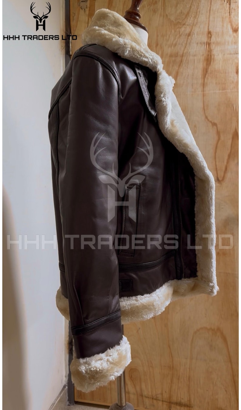 Pode incluir: Casaco de couro castanho com forro e acabamento em pele de carneiro creme. O casaco tem um estilo aviador cl&aacute;ssico com gola larga e fecho de correr. O texto "HHH TRADERS LTD" &eacute; vis&iacute;vel.