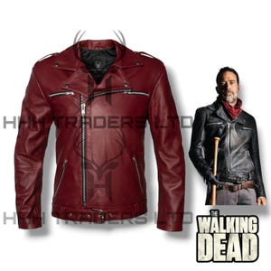 May include: A burgundy leather motorcycle jacket with a classic asymmetrical zip closure, multiple zippered pockets, and a belted waist. The jacket features a notched collar and shoulder epaulets. The image also includes a person wearing a black leather jacket and the Walking Dead logo.