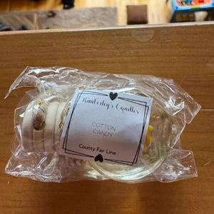 May include: A clear glass car air freshener bottle with a wooden cap and a white label that reads Kimberly's Candles, Cotton Candy, and County Fair Line, all enclosed in a transparent plastic bag with a hanging cord.