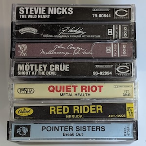 May include: A stack of seven vintage cassette tapes. Titles include "Stevie Nicks: The Wild Heart", "Flashdance", "John Cougar Mellencamp", "Motley Crue: Shout at the Devil", "Quiet Riot: Metal Health", "Red Rider: Neruda", and "Pointer Sisters: Break Out".