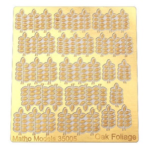 Può includere: Un foglio di metallo color oro con più disegni ritagliati di foglie di quercia. Il foglio è etichettato "Matho Models 35005 Oak Foliage".