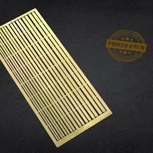 Peut inclure: Une grille métallique dorée de forme rectangulaire avec un motif quadrillé, sur fond sombre. La grille est inclinée, révélant ses lignes parallèles. Un tampon circulaire avec le texte "PHOTO-ETCH" est visible.