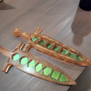 Peut inclure: Deux moules en résine en forme de poignard avec un motif en nid d'abeille. Les moules sont remplis de résine pailletée verte.