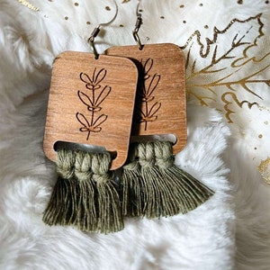 May include: A pair of wooden earrings with a green tassel. The earrings are rectangular and have a floral design carved into the wood.
