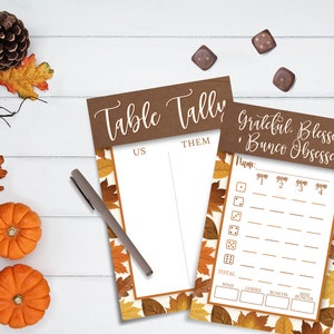 Op de afbeelding: Twee printbare scorekaarten voor een Bunco-spel met een herfstthema. De scorekaarten hebben een bruine achtergrond met een witte rand en een patroon van oranje en gele bladeren. De tekst op de scorekaarten luidt "Table Tally" en "Grateful, Blessed, Bunco Obsessed".