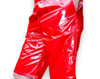May include: Bright red, shiny shorts with an elastic waistband and pockets. The shorts have a glossy, wet look and appear to be made of a synthetic material. The shorts are knee-length and have a relaxed fit.