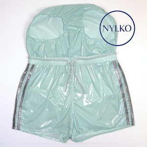 May include: A mint green glossy vinyl shorts set featuring a high-waisted design with an elastic waistband, a drawstring, and silver reflective side stripes. The garment includes the text NYLKO printed in a dark blue circle on the upper section.