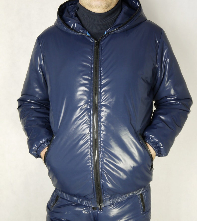 May include: A navy blue, hooded jacket with a shiny, quilted appearance. The jacket has a full-length black zipper, two front pockets, and a matching navy blue bottom. The jacket is part of a two-piece set.