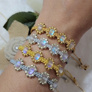 May include: Four macrame bracelets with iridescent moonstone-like beads and gold or silver accents are displayed on a wrist. The bracelets have a floral design with a neutral background. The bracelets are handmade.