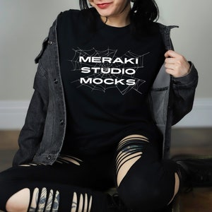 May include: A black long-sleeved shirt with a spiderweb graphic and the text "MERAKI STUDIO MOCKS" in white.