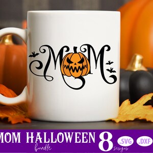 K&ouml;nnte beinhalten: Eine wei&szlig;e Keramiktasse mit einem schwarzen Design des Wortes "MOM" mit einem K&uuml;rbisgesicht in der Mitte. Die Tasse ist von Herbstbl&auml;ttern und K&uuml;rbissen umgeben.