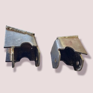 May include: Two metal brackets with a rusty finish. The brackets are shaped like a U with a flat top and bottom. They are likely used for mounting or supporting something.