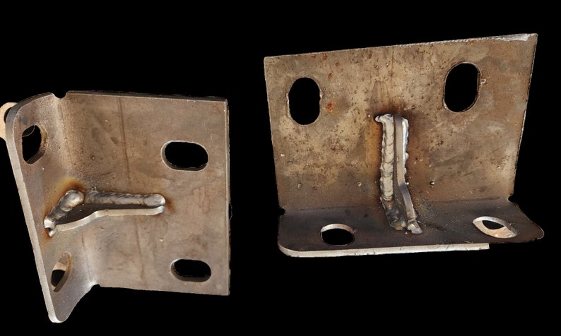 K&ouml;nnte beinhalten: Zwei Metallwinkel mit geschwei&szlig;ten Verbindungen und mehreren L&ouml;chern. Die Winkel sind aus rauh, braunem Metall.