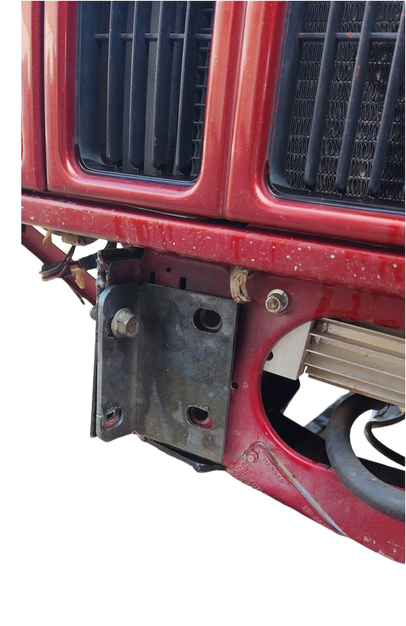K&ouml;nnte beinhalten: Nahaufnahme der vorderen Sto&szlig;stange eines roten Autos mit einem befestigten Metallhalter. Der Halter hat eine Schraube und einige L&ouml;cher. Die Sto&szlig;stange hat einen schwarzen Kunststoffgrill und ein silbernes Metallteil.