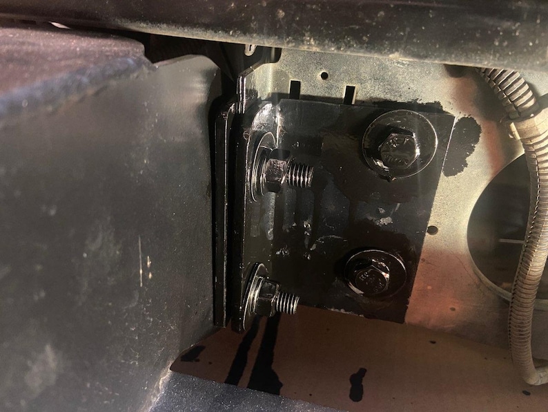 K&ouml;nnte beinhalten: Nahaufnahme einer schwarzen Metallhalterung mit zwei Schrauben und Unterlegscheiben. Die Halterung ist an einer gr&ouml;&szlig;eren Metalloberfl&auml;che befestigt.