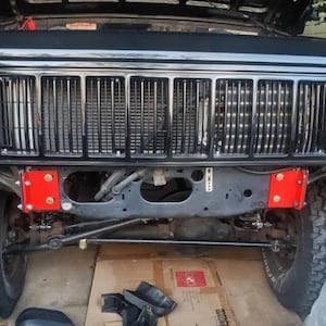 K&ouml;nnte beinhalten: Schwarzer Jeep Cherokee mit schwarzem K&uuml;hlergrill und roten Metallsto&szlig;stangen. Der Jeep steht auf einer Betonfl&auml;che.