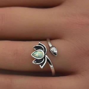 May include: A silver ring with a white opal lotus flower design. The ring is adjustable and wraps around the finger.