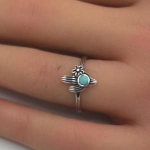 May include: A silver ring with a turquoise stone and a cactus design.