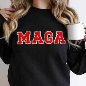 May include: Black sweatshirt with the text "MAGA" in red letters with gold glitter outlining.
