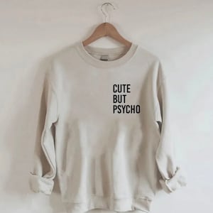K&ouml;nnte beinhalten: Ein hellbeiger Pullover mit dem Aufdruck "CUTE BUT PSYCHO" in Schwarz auf der Vorderseite.