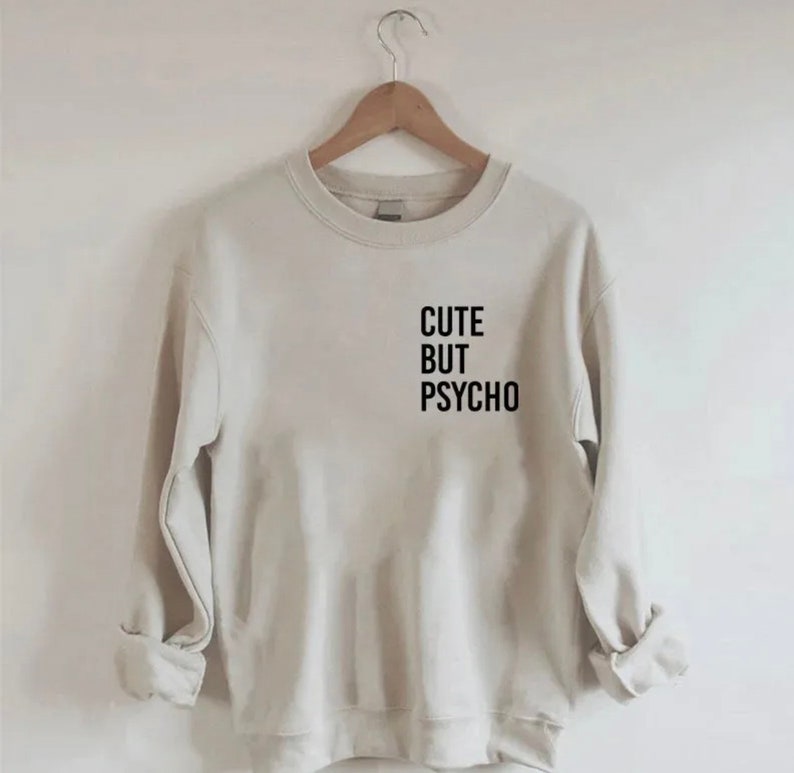 K&ouml;nnte beinhalten: Ein hellbeiger Pullover mit dem Aufdruck "CUTE BUT PSYCHO" in Schwarz auf der Vorderseite.