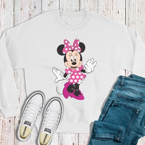 May include: White sweatshirt featuring a pink and white Minnie Mouse design. The sweatshirt has a crew neck and long sleeves.