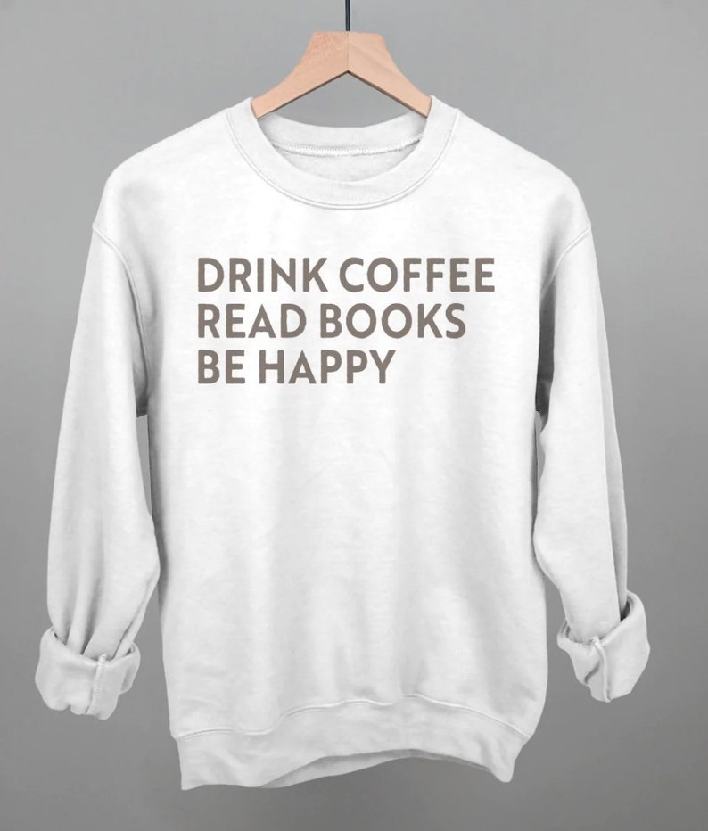 以下が含まれることがあります： 「Drink Coffee Read Books Be Happy」という茶色の文字が書かれた白いスウェットシャツです。