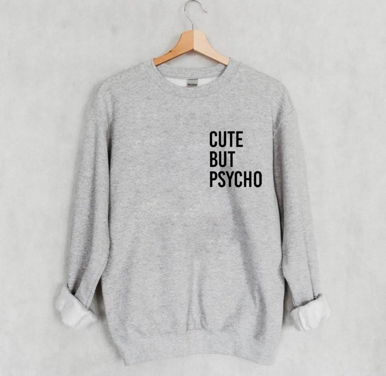 K&ouml;nnte beinhalten: Grauer Pullover mit dem Aufdruck "CUTE BUT PSYCHO" in Schwarz auf der Vorderseite.
